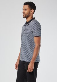 Lyhythihainen polo-paita tummansinisessä ja valkoisessa timanttikuviossa, mustalla kauluksella ja napilla. Valmistettu hengittävästä kankaasta mukavuutta varten.