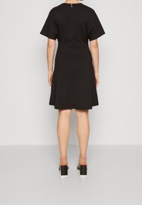Czarna sukienka z krótkimi rękawami i rozkloszowanym dołem. Gładki materiał z zamkiem błyskawicznym z tyłu i okrągłym dekoltem. Połączona z butami na słupku.