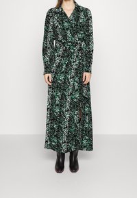 Långärmad omlottklänning i svart och grön leopardmönster, med något definierad midja och en sidoklyvning. Matchas med svarta stövlar.