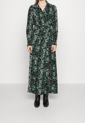 Robe portefeuille à manches longues en imprimé léopard noir et vert, avec une taille légèrement marquée et une fente sur le côté. Associée à des bottes noires.