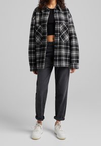 Svart och grå rutiga flanellskjortjacka med två bröstfickor, bärs över en svart crop top och matchas med mörka jeans och vita sneakers.