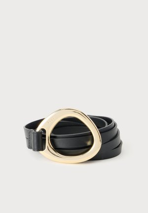 Ceinture en cuir noire enroulée avec une grande boucle métallique dorée irrégulière sur un fond clair uni.