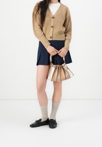 Knit camel cardigan with buttons, navy pleated skirt, cream and beige handbag with a chain handle, and light beige socks with black shoes.