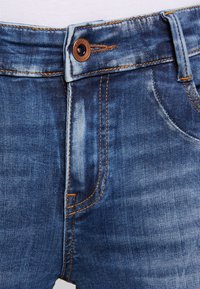 Jeans de mezclilla azul con un clásico diseño de cinco bolsillos, costuras naranjas contrastantes y un cierre de botón metálico en la cintura.