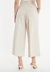 Weite Hosen in Creme mit vertikalen Streifen. Sie verfügen über eine hohe Taille, seitliche Taschen und eine glatte Stoffoberfläche. Einfarbiger Saum.