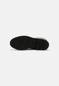 Suela de goma negra con un patrón de banda de rodadura hexagonal, que presenta profundas ranuras para tracción y durabilidad. Elementos de diseño robustos y funcionales son visibles.