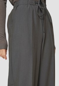 Dunkelgraue Hose mit elastischem Bund und Kordelzug, ausgestattet mit Seitentaschen und einem glatten, strukturierten Stoff. Designed für einen lässigen Sitz.