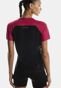 Sportovní top s růžovým panelem na ramenou a zádech a černým tělem. Texturovaná látka se síťovinou pro prodyšnost.