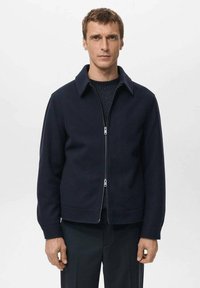 Granatowa kurtka zapinana na zamek z kołnierzem, wykonana z fakturowanej tkaniny. Posiada prosty krój i dwie kieszenie z przodu.