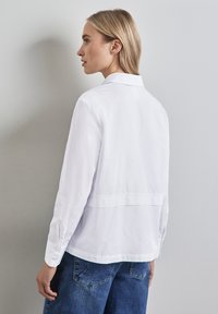 Camicia bianca a bottoni realizzata in tessuto leggero, caratterizzata da una vestibilità comoda, maniche lunghe e un pannello sulla schiena per un tocco di eleganza.