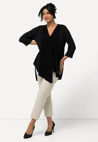 Top nero fluente con scollatura a V e maniche 3/4 abbinato a pantaloni cremosi a gamba affusolata. Il modello indossa tacchi alti neri e posa su uno sfondo neutro.