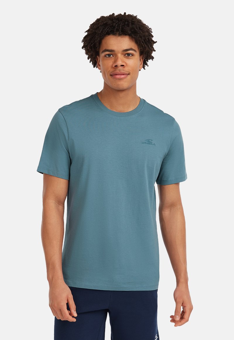 Teal kortærmet T-shirt lavet af blødt stof, med rund halsudskæring og et diskret logo på brystet, sammen med navy shorts.