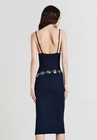 Robe midi côtelée bleu marine avec fines bretelles, dotée d'un dos plongeant et d'une chaîne décorative argentée à la taille. Texture lisse et silhouette ajustée.