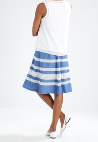 Jupe rayée bleue avec des détails en dentelle blanche, associée à un haut sans manches blanc. Présente un design évasé et une coupe à mi-mollet. Chaussures plates blanches.