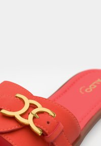 Korallfarbene Slide-Sandale mit glatter Textur, zwei goldenen runden Schnallen und einer gepolsterten Innensohle mit Markenlogo.