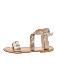 Gouden metallic sandalen met twee brede banden en een gespsluiting rond de enkel. De zool is plat met een natuurlijke leren afwerking.