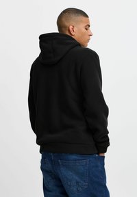 Black hooded sweatshirt with a soft texture, featuring a relaxed fit and ribbed cuffs, paired with blue denim jeans.