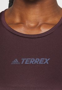 Primer plano del cuello y la parte superior del pecho vistiendo una camiseta Adidas Terrex de color púrpura oscuro, con el logo centrado debajo del cuello.