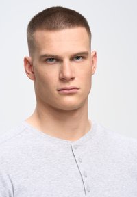 Camiseta henley gris con cuello redondo y tapeta de cuatro botones, fabricada en una tela texturizada, con mangas cortas y corte ajustado.