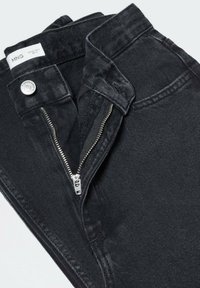 Jean en denim noir avec zip, fermeture à bouton et taille structurée avec une surface légèrement texturée. Étiquette visible à l'intérieur.