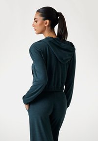 Gekürzter Hoodie in Dunkeltürkis, aus weichem Stoff, mit Kapuze, elastischem Bund und langen Ärmeln, kombiniert mit passenden Hosen.