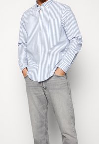 Blauw-wit gestreepte overhemdbloes met een kraag, lange mouwen en een borstzak, gecombineerd met lichtgrijze jeans.
