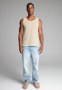 Top de tirantes acanalado beige, jeans de mezclilla azul claro y zapatos deslizables color marrón claro. El conjunto presenta un ajuste relajado y una textura suave.