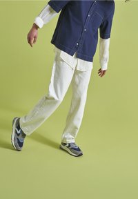 Chemise à manches courtes bleu marine sur une chemise à manches longues blanche, associée à un pantalon blanc et des baskets bleu-gris. Tissu lisse avec des coutures contrastantes.