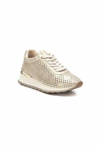 Zapatilla deportiva beige con parte superior perforada, cordones planos y acento metálico en el talón; fabricada en tela y goma, con una suela acolchada.