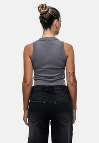Grijze, cropped tanktop met een ronde hals, gemaakt van zacht materiaal, gecombineerd met hoge zwarte denim broeken met achterzakken.