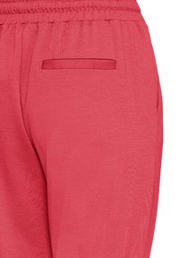 Pantalon léger rouge à coupe décontractée, avec une taille élastique et une poche latérale discrète. Tissu lisse et texturé.
