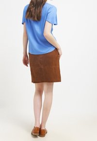 Camicia corta blu abbinata a una gonna in suede marrone, con una leggera forma a A. Scarpe marroni completano l'outfit.