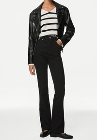 Chaqueta de cuero negra para motociclista sobre un suéter de rayas blancas y negras, combinada con pantalones vaqueros negros acampanados de talle alto y zapatos negros.