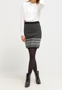 Svartvitt mönstrad kjol med åtsittande midja, featuring geometriska mönster. Kombinerad med en vit blus och svarta ankelstövlar.