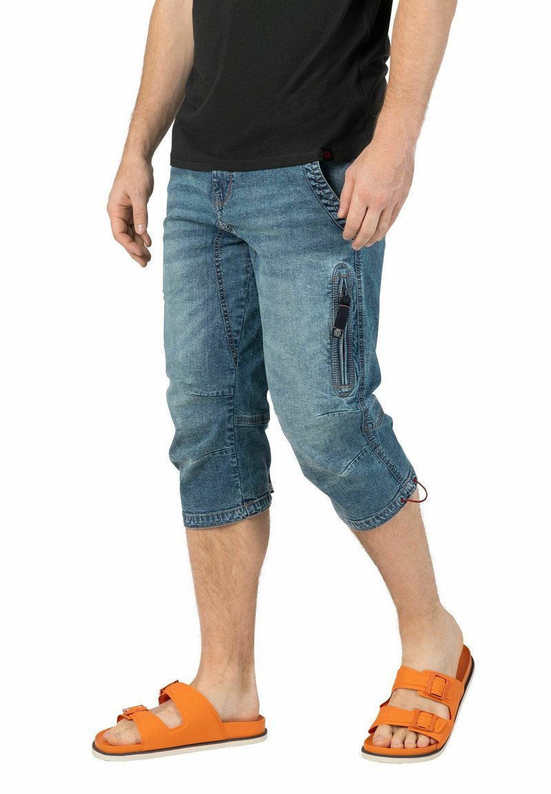 Denim-Capri-Hosen in einem verblassten Blauton, mit seitlicher Reißverschlusstasche und Kordelzug am Saum, kombiniert mit orangen Slidesandalen.