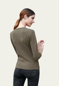 Haut olive à manches longues avec un col rond, coupe slim et texture douce, associé à un jean en denim foncé avec poches arrière.