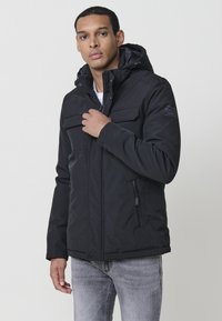 Juoda zip-up striukė su gobtuvu, turi keturis priekinės kišenes, lygų paviršių ir šiek tiek paminkštintą dizainą šilumai.