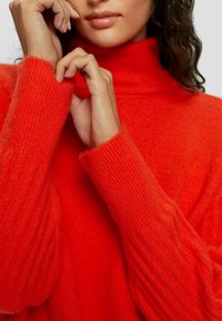 Roter Rollkragenpullover aus weichem, strukturiertem Stoff; mit gerippten Ärmeln und geradem Schnitt für eine bequeme Passform.