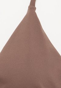 Gros plan d'une section triangulaire en tissu marron avec une couture et une boucle étroite en haut sur un fond blanc uni.