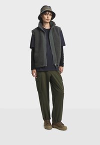 Veste en polaire grise, t-shirt bleu marine, pantalon cargo olive et bottes marron. Chapeau seau gris et bleu marine. Comprend une fermeture éclair à l'avant et des poches latérales.