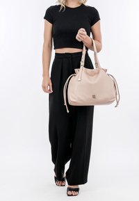 Pink leather handbag with gold hardware, drawstring sides, and a logo on the front, held by a person wearing a black crop top and wide-leg pants.
