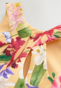Gelbes Oberteil aus Stoff mit floralen Mustern, das lebhafte rosa, rote und blaue Blumen sowie grüne Blätter zeigt. Mit klaren Knopfdetails.