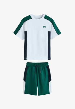 Valge ümmarguse kaelusega t-särk roheliste ja mustade värvilahendustega, kombineeritud roheliste lühikeste pükstega, millel on mustad ja valged külje paneelid ning pingutuspaelaga vöökoht.