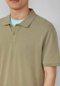 Beige Polohemd aus strukturiertem Stoff, mit klassischem Kragen, zwei Knöpfen und einem kleinen gestickten Logo auf der Brust.