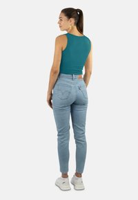 Türkises, ärmelloses Oberteil kombiniert mit hoch taillierten hellblauen Jeans. Verfügt über eine figurnahen Schnitt und ein minimalistisches Design, getragen mit weißen Turnschuhen.