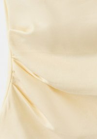 Tissu froncé couleur crème avec des plis doux et une texture subtile, montrant des détails en gros plan du matériau de vêtement.