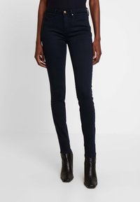 Jeans skinny azul oscuro con cintura de altura media, confeccionados en tela de mezclilla. Presentan botones en tono dorado y una textura suave.
