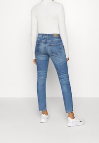 Blå denimjeans med en figursydd design, två bakfickor och en ljus tvätt. Sammanfattad med en vit långärmad topp och vita sneakers.