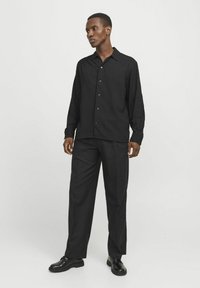 Zwarte button-up shirt met een gestructureerde afwerking, lange mouwen en een klassieke kraag, gecombineerd met losse zwarte broek en zwarte schoenen.