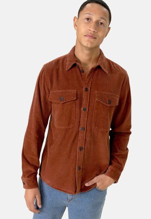 Brown corduroy shirt featuring two chest pockets, button closure, and a pointed collar, paired with light blue denim jeans.